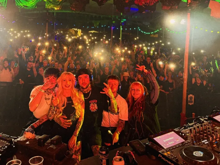 Both DJs at the booth with the whole room lit up behind them
