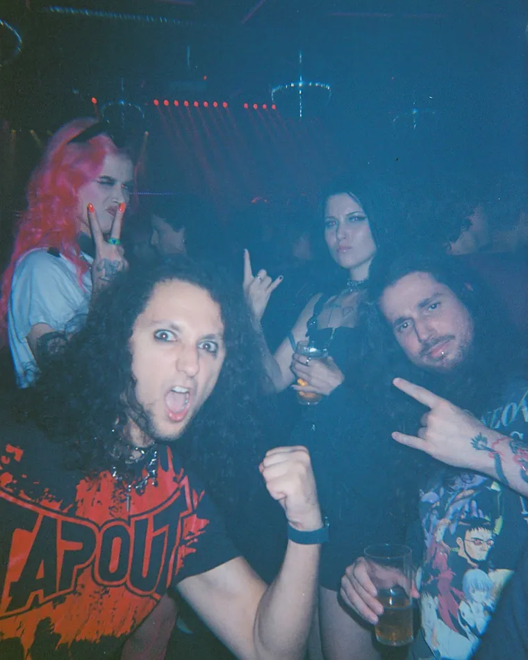 Three mates close together under the flash, horns up, near the end of the night